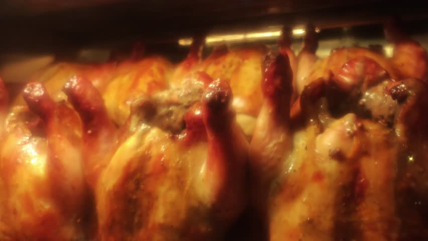 Chickens roasting. Close up whole chickens roasting on rotating rotisserie inside industrial oven. Golden skin glistens under heat. Food production roasting process and commercial kitchen operations.
