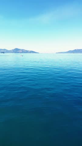 Wide view of calm blue ocean with distant mountains and clear sky, showcasing a peaceful natural seascape
