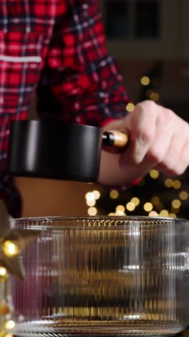 Person in plaid shirt pours milk from a black measuring cup into a clear glass bowl, creating a creamy mixture for a hot chocolate drink preparation process