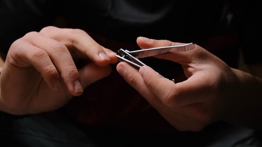 Close up young male hands using nail clippers to trim fingernails. Personal grooming and self care. Male manicure done independently. Regular hand care and hygiene routine.