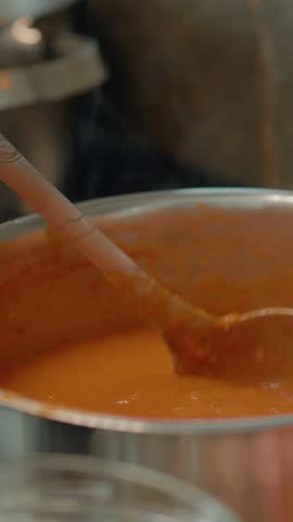 Vertical Screen: A woman carefully transfers a rich homemade tomato sauce with onion and basil from a saucepan to glass jars, preparing for storage. The kitchen is bright and welcoming.