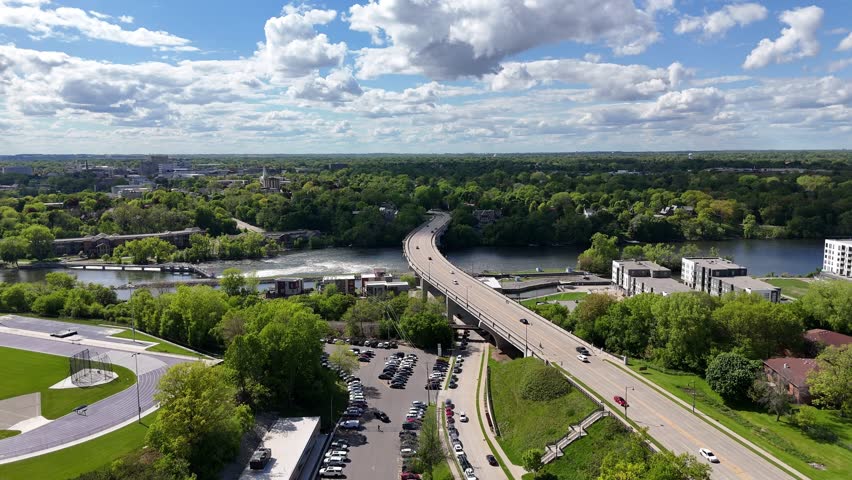 High push Drone shot approaching Bridge over Fox River in Appleton Wisconsin USA.  Dam and Bridge in the distance with Cars driving.  Blue Skies, with scattered clouds through the sunshine on summer day. New Condos and apartments on the right hand side.