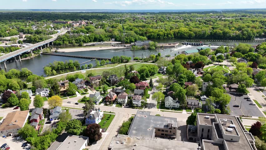 Right to Left Drone shot turning into orbital of Fox River and Downtown Appleton Wisconsin USA.  Shots of the river, bridge, dam and Hydro Electric buildings in the distance. Cars and traffic on Summer Day.