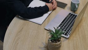 High angle view of a focused young student taking notes in a notebook at her desk, surrounded by a laptop and smartphone, emphasizing the importance of learning about online safety and cybersecurity - Powered by Shutterstock - Get 15% off with code: PIKWIZARD15