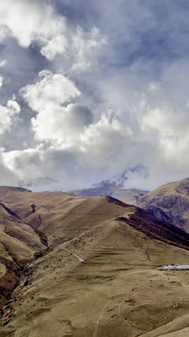 High autumn mountains with clouds drifting over the peaks and snow covering the upper areas, creating a calm and cinematic natural scene.