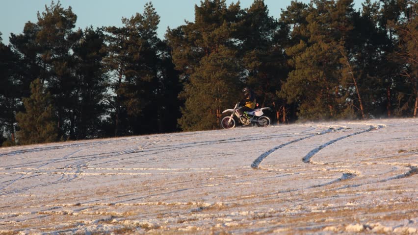 Exhilarating winter sports scene: dirt bike rider powerfully drives through a snowy landscape, kicking up a dramatic cloud of snow powder in a thrilling display of skill and adventure, back lit by
