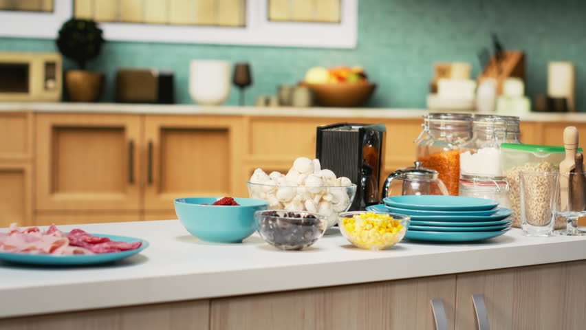 Comfortable kitchen setup with pizza ingredients on a modern countertop. Bowls of cheese, tomatoes and pepperoni sit beside spices and kitchenware, ready for a fun weekend activity of cooking.