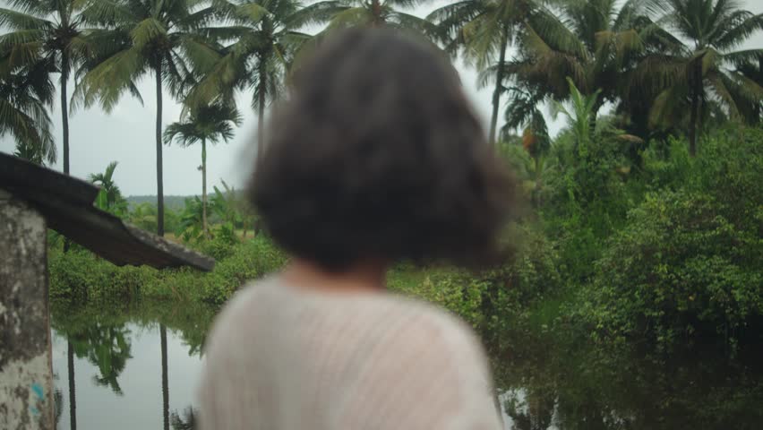 Woman standing by lush river, serene tropical setting, peaceful mood