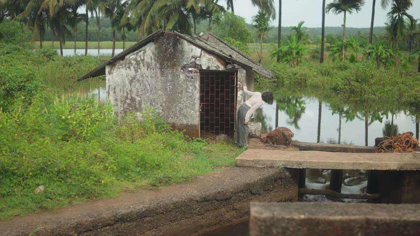 Zoom in shot toward a small rural house near water and greenery, showing quiet countryside life and natural surroundings.