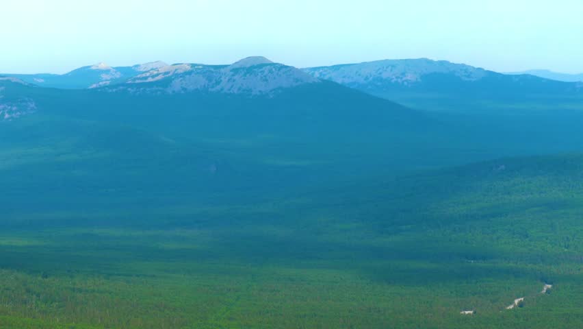 view of the vast green forest and rolling mountains of the Southern Urals region in Russia on a clear day. The landscape captures the natural beauty and wilderness of the remote area, possibly featuri