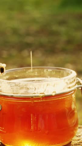 A close-up shot of a hand stirring a jar of delicious golden honey with a honey dipper, with bees flying around, creating a delightful natural scene