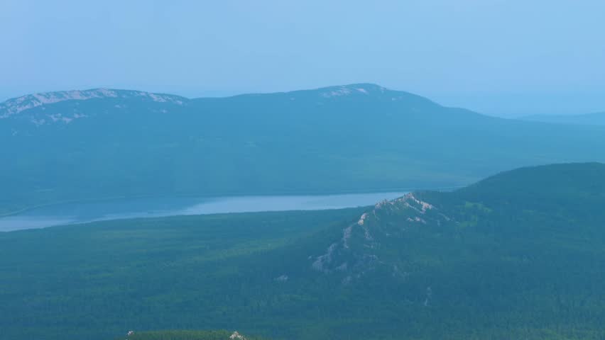 An extraordinarily beautiful summer landscape captured at dusk, featuring a serene mountain lake nestled among several parallel ridges of the Southern Urals, Russia.