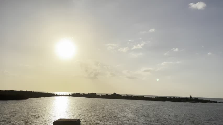 Point of view shot driving on a bridge over the ocean during a beautiful sunset in a tropical location, with the sun reflecting on the calm water and a few clouds dotting the sky