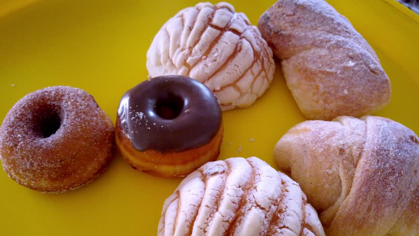 Hand using tongs to select pastry from a bakery tray with assorted sweet bread.