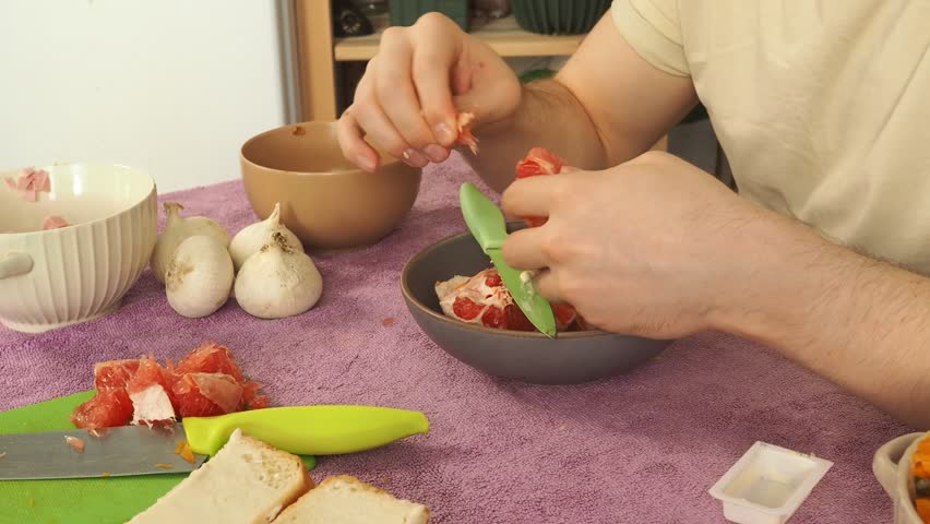 A man peels a ripe grapefruit for breakfast.