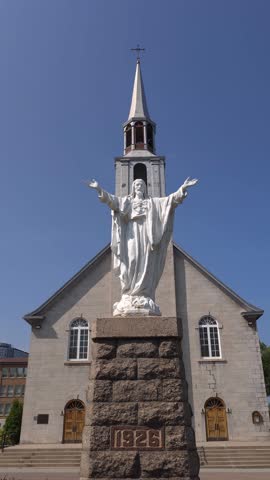A large white statue of Christ the King stands prominently in front of a stone church with a steeple. The statue is positioned on a stone pedestal with the year 