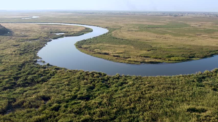 A gentle bend in the Cubango River flows through wetlands near Shakawe in the Okavango Delta, Botswana, surrounded by grassy floodplains and calm water channels.