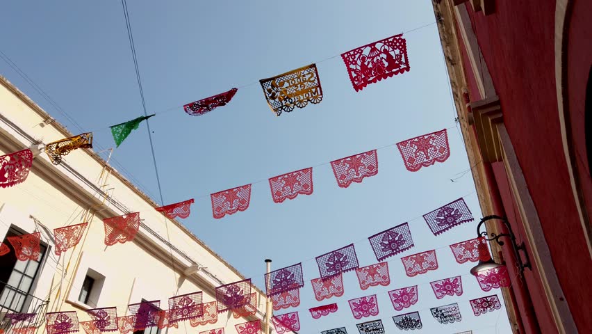 Decorative papel picado flags hanging above a street creating a festive cultural atmosphere during daytime.