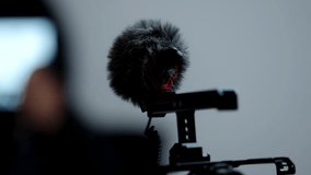Close-up of a shotgun microphone with furry windscreen mounted on a camera rig during an indoor interview setup, capturing dialogue with shallow depth of field and studio lighting. - Powered by Shutterstock - Get 15% off with code: PIKWIZARD15