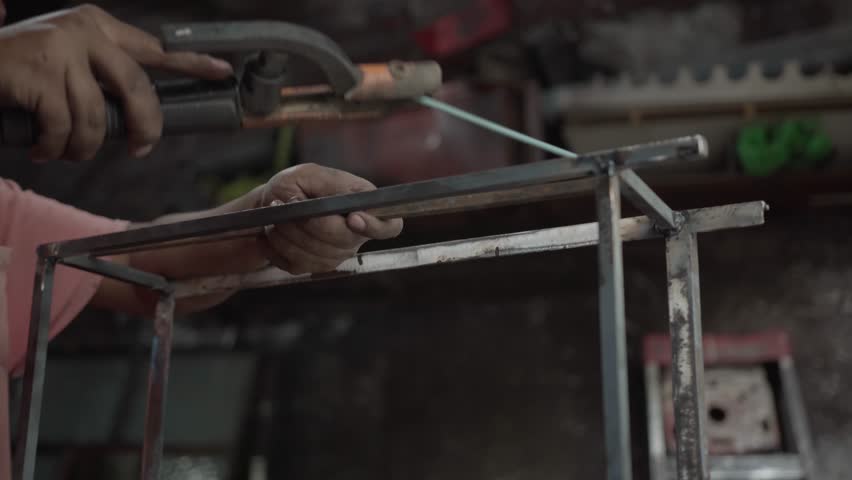 Professional metal worker using an arc electrode welder to fabricate metallic structure with wild sparks in workshop