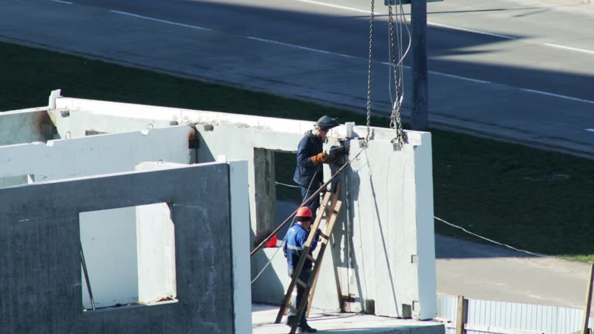 One Worker Welds As Colleague Climbs Ladder To Help.