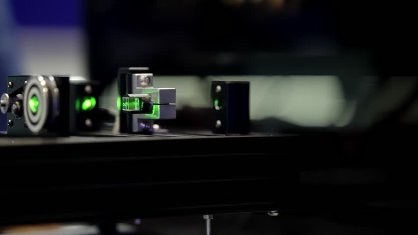 Precision laser optics bench with green beam alignment through mirrors, mounts, and beam splitters on an optical rail for laboratory photonics equipment and measurement