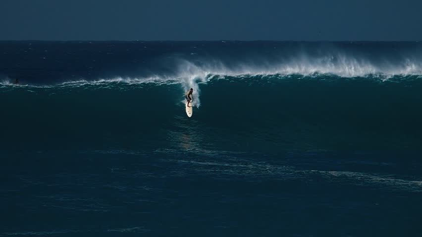 Big wave surfing in Hawaii on Waimea Bay. Person surfs the huge ocean wave breaking on the Hawaiian shore in Waimea Bay. Surfer rides the big wave in Hawaii. Oahu island