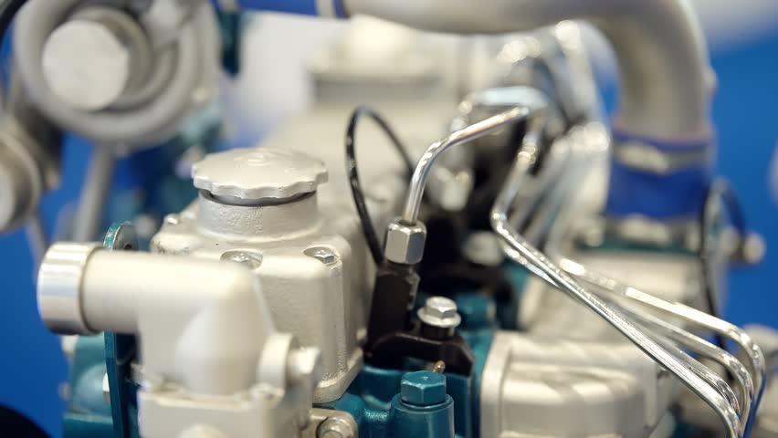 Macro view of an industrial engine assembly with metallic pipes, valves, and fuel lines, highlighting precision components, fittings, and complex tubing against a blue background