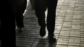Low-angle glimpse of pedestrians walking across a sunlit brick sidewalk, their legs casting long shadows while glass surfaces mirror their movement in a quiet urban scene - Powered by Shutterstock - Get 15% off with code: PIKWIZARD15