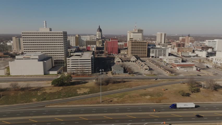 Aerial drone shot moving right to left showing the Kansas State Capitol with highway traffic in Topeka. Cinematic establishing footage highlighting government, transportation, urban infrastructure.