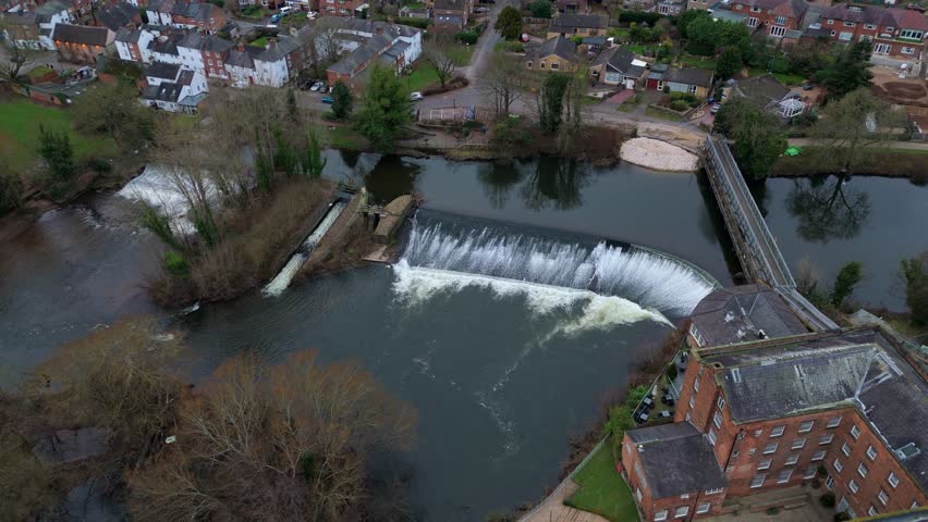 Aerial view of a weir cascading into the river alongside a bridge, contrasting with the adjacent building and the town beyond, Derby, England, United Kingdom.