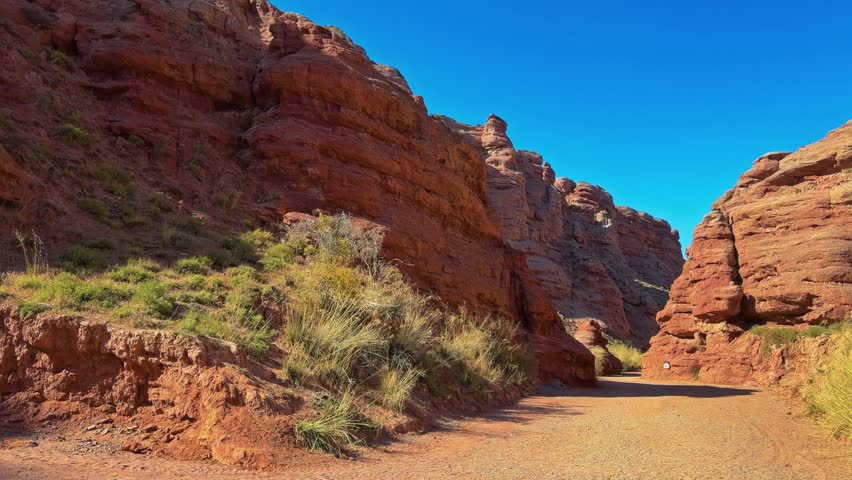 Pingshan Lake Grand Canyon, Zhangye, Gansu Province, China - A Narrow Dirt Path Winds Between Towering Red Sandstone Cliffs Under a Deep Blue Sky - Pan Right Shot