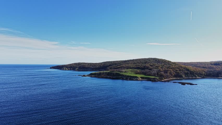 Bright blue waters stretch to the shoreline, revealing lush green hills under a clear sky. This tranquil coastal scene captures nature