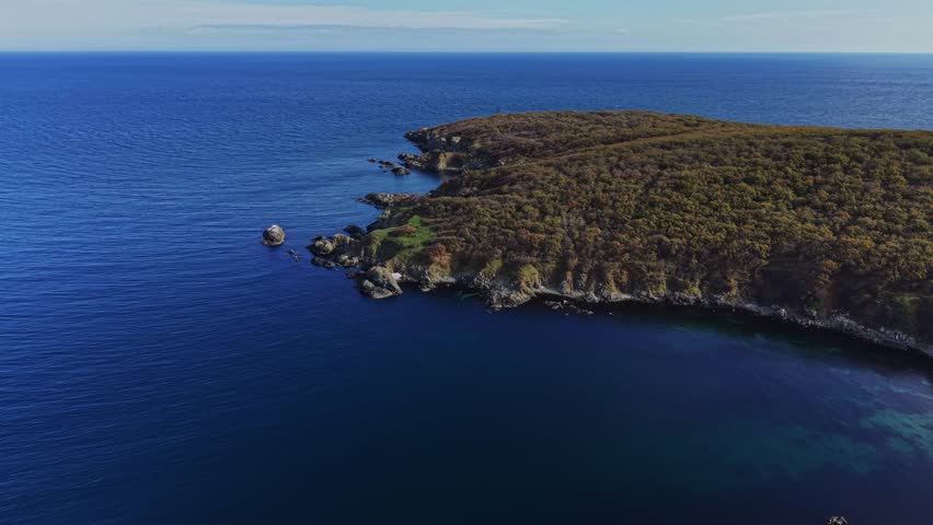 The coastline features steep cliffs covered in trees, with clear blue water surrounding the rocky outcrops. This stunning landscape showcases nature