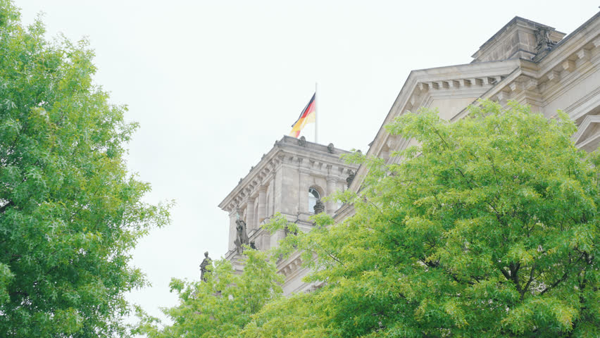 Slow camera pan to the Bundestag in Berlin (Germany) with trees in the foreground. The German flag flies on the roof.