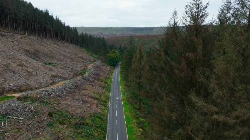 Camper van driving along empty rural road surrounded by trees and hills under cloudy sky. Vehicle moving through scenic valley emphasizing road safety and traffic awareness in remote infrastructure