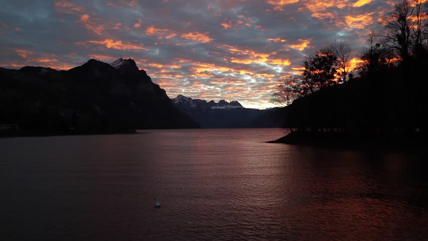 Sunset sky reflecting on lake with dark alpine mountain outlines