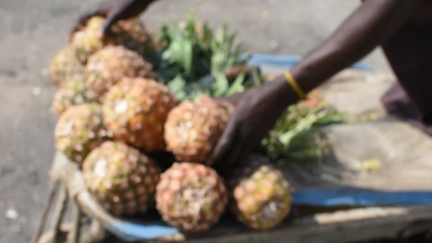 Close-up video of hands arranging fresh pineapples for sale at a local street market.