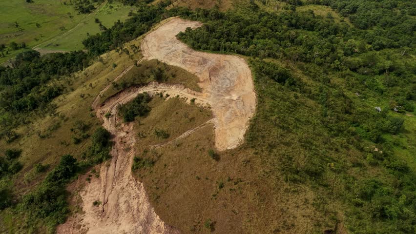Striking overhead perspective captures major roadway construction project carving through elevated terrain near Busuanga Airport in Decalachao barangay, Coron municipality, Palawan province, Philippines. Newly excavated serpentine route displays raw earth tones contrasting dramatically against surrounding vegetation, showcasing active infrastructure development phase. Heavy equipment tracks visible across freshly graded surfaces.
Winding alignment follows natural topography, demonstrating careful engineering approach to mountainous landscape challenges. Mixed vegetation patterns reveal transition zones between cleared grasslands and dense forest patches, while strategic route placement minimizes environmental disruption. This significant connectivity project aims to improve regional accessibility, supporting tourism growth and local economic opportunities around busy airport facility.
Dramatic elevation changes create dynamic visual composition emphasizing scale of undertaking required for island transport networks. Perfect stock content for projects exploring infrastructure expansion, civil engineering documentation, regional development initiatives, environmental impact studies, or Philippine provincial modernization efforts. Ideal for construction industry features, government planning presentations, investment opportunity materials, or documentaries examining balance between progress and ecological preservation in Southeast Asian island environments requiring improved ground transportation systems.