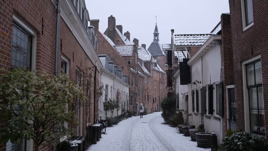 Person walking around in the historic city center of the city of Amersfoort in the Netherlands in winter during snowfall with Dutch houses and architecture