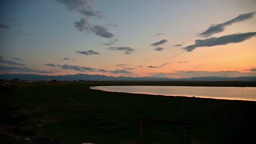 A ground-based panorama of a lake at sunset amidst the steppe with mountains in the background. Smooth panning.