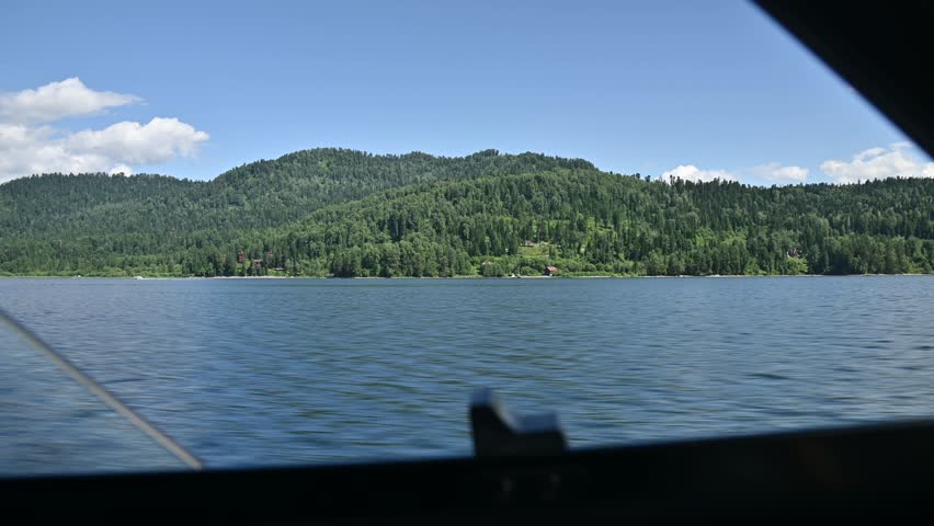 POV view from the side window of a motorboat moving at speed across a large mountain lake in the forest. Watercraft travel on mountain lakes.