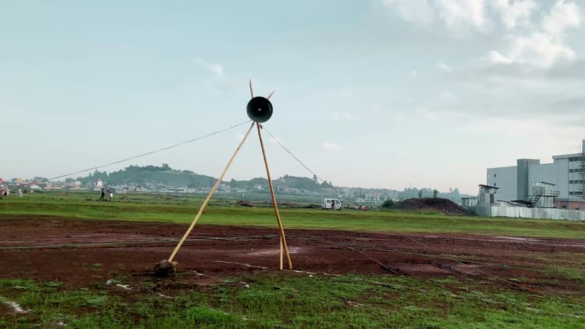 Semi-orbit drone shot circling a large speaker mounted on a wooden tripod in an open field during Eid al-Adha. Captures festive atmosphere, outdoor setup for Eid announcements, and cultural celebration, created on 12 July 2024 for editorial and cultural video use.