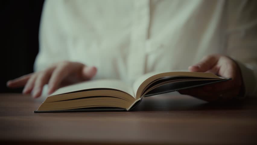 A close-up shot of hands interacting with an open book, suggesting a moment of focused reading or study