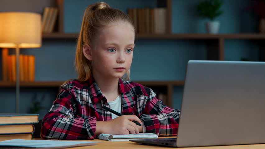 Caucasian kid daughter girl writing online studying raising hand ready to answer online teacher smiling clever school child pupil learning distant from home laptop video call e-learning write notes