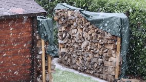 Heavy snow falling on stacked firewood logs covered with green tarp in garden - Powered by Shutterstock - Get 15% off with code: PIKWIZARD15