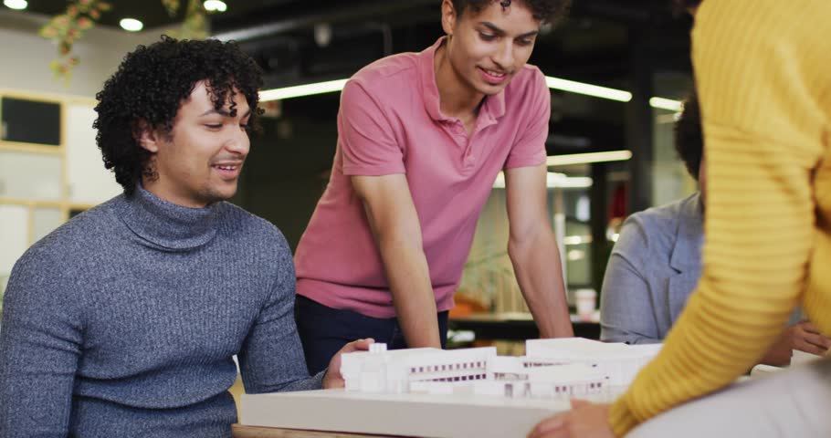 Design team tuning model, lead pointing while yellow reaching starting placing, icons marking model. Architectural, collaboration, prototyping, studio, planning, brainstorming, groupwork