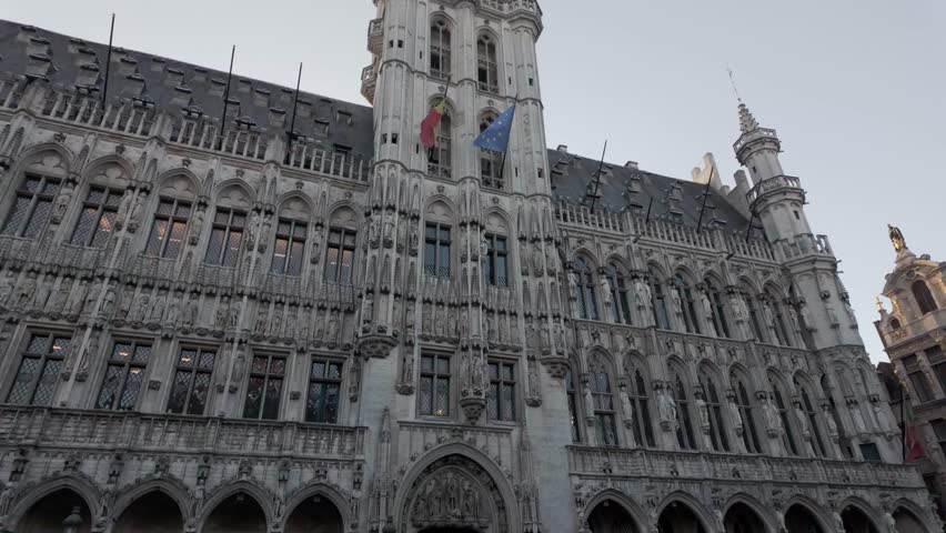 Video of an upward pan of the Brussels Town Hall tower located in Grand Place, Belgium. The clip shows the beautiful Gothic architecture and intricate details of the historic building against a clear blue sky, capturing the elegance and grandeur of this famous European landmark.