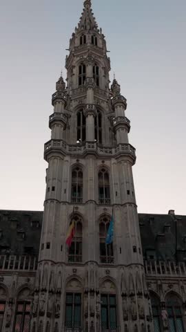 Video of the Brussels Town Hall tower at Grand Place, Belgium, showing the Belgian and European Union flags gently waving in the wind. The clip highlights the Gothic architecture and elegant details of this famous European landmark on a calm, bright day.