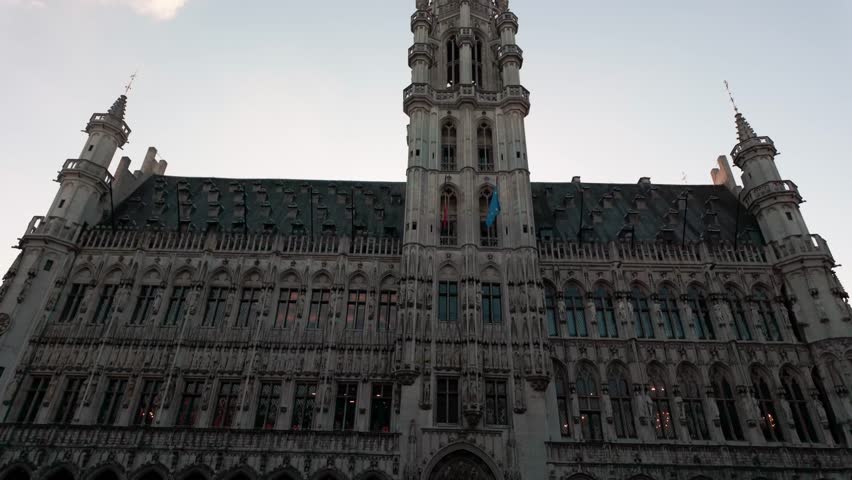 Video of an upward pan of the Brussels Town Hall in Grand Place, Belgium, filmed at sunset with the sun behind the building. The clip highlights the Gothic architecture and spire of the historic landmark, silhouetted against a glowing sky in the evening light.